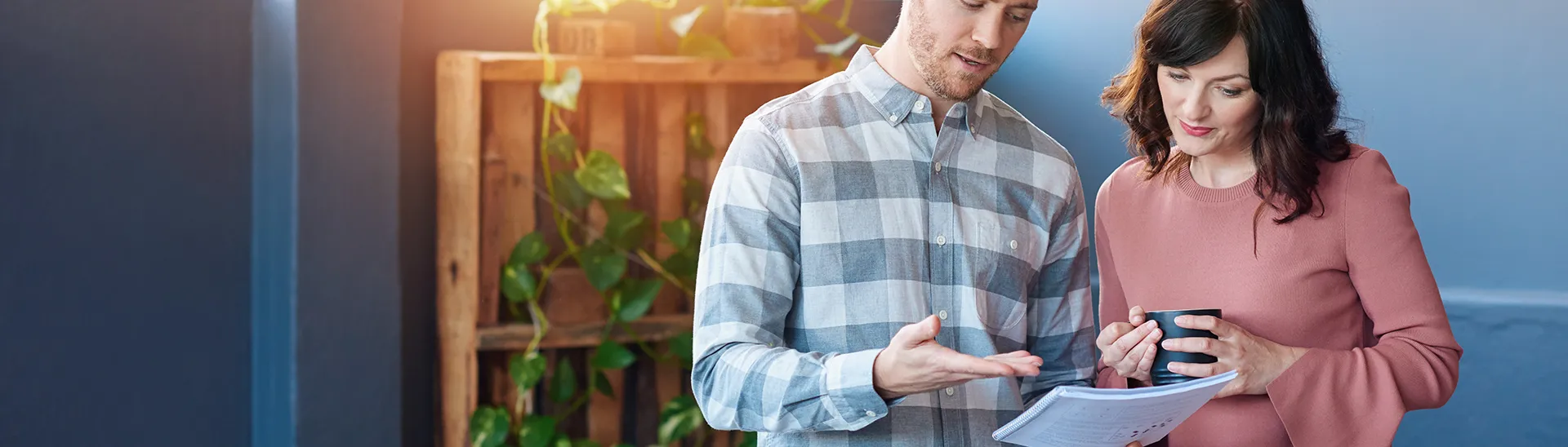A couple looking down at a tablet with a planting rack with green plants it in the background.