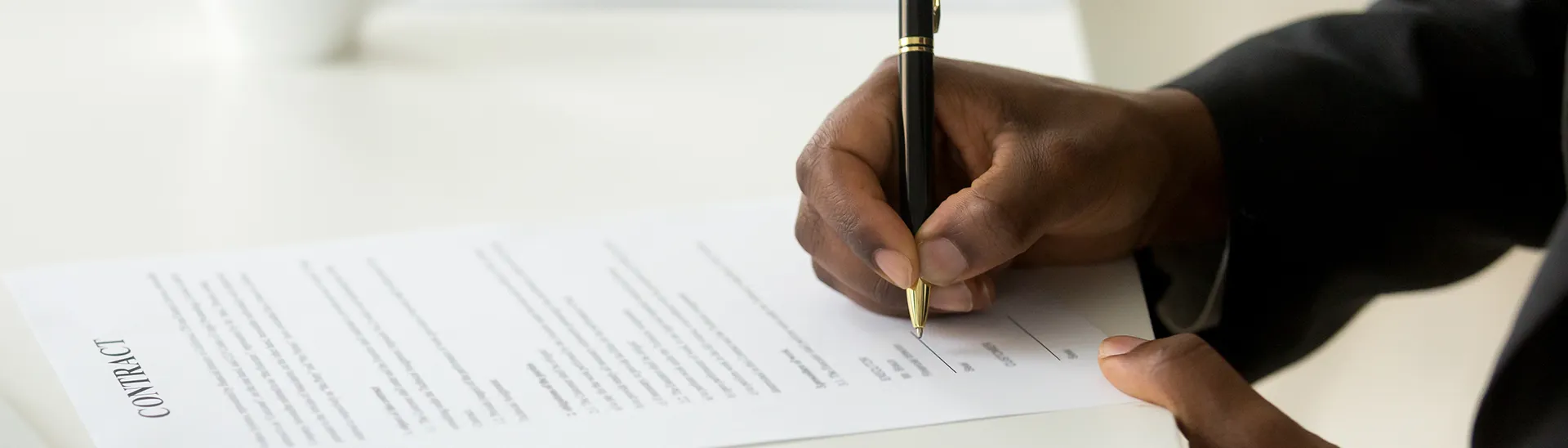 Black man's hand holding a pen while writing on a piece of paper.