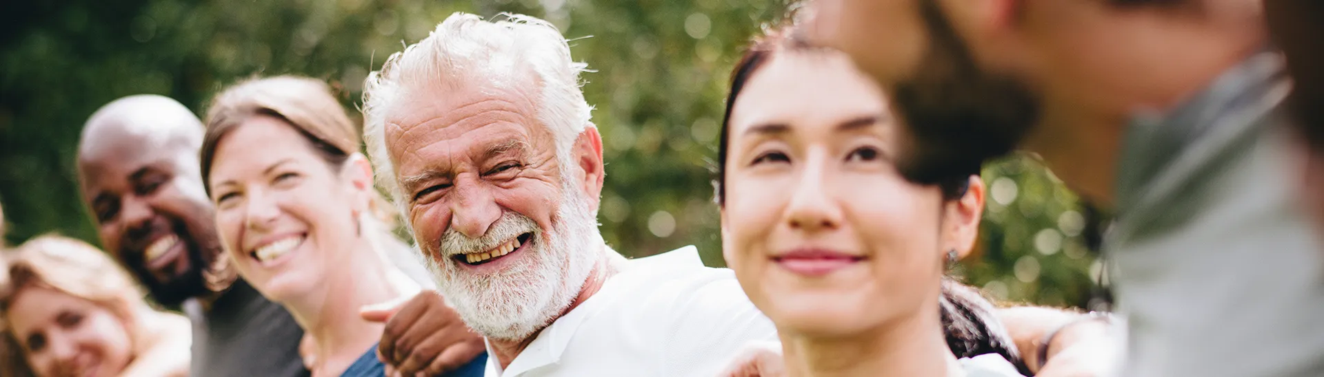 Group of individuals of different ages and races with their arms around each other smiling and laughing together