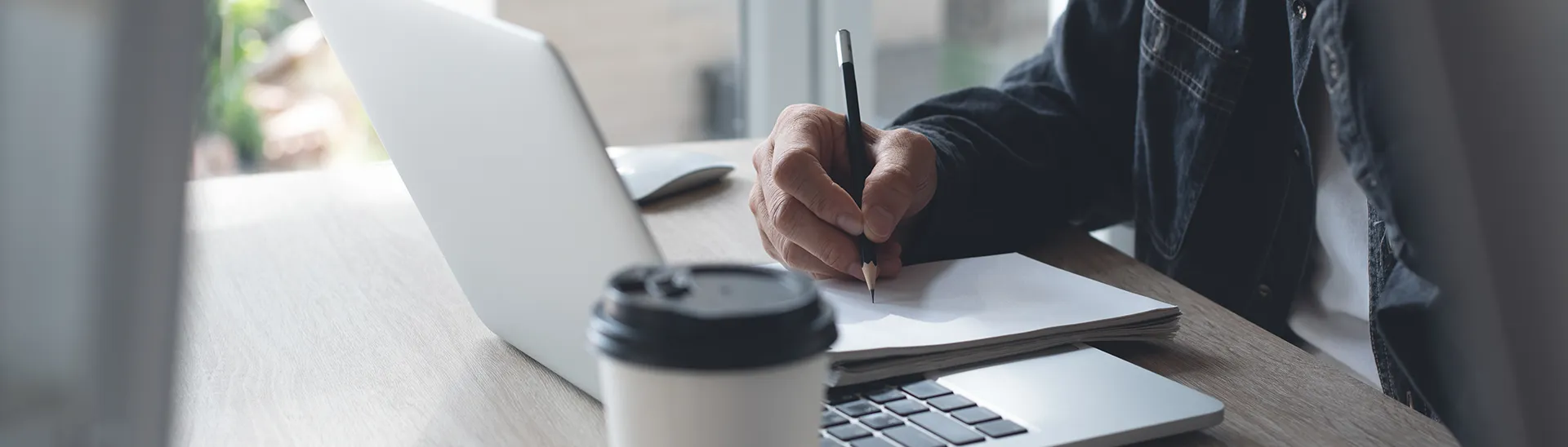 Older man talking on the phone while looking at his laptop screen and taking notes