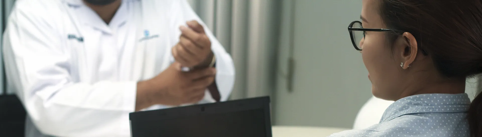 Woman on computer with a doctor sitting across from her in the background