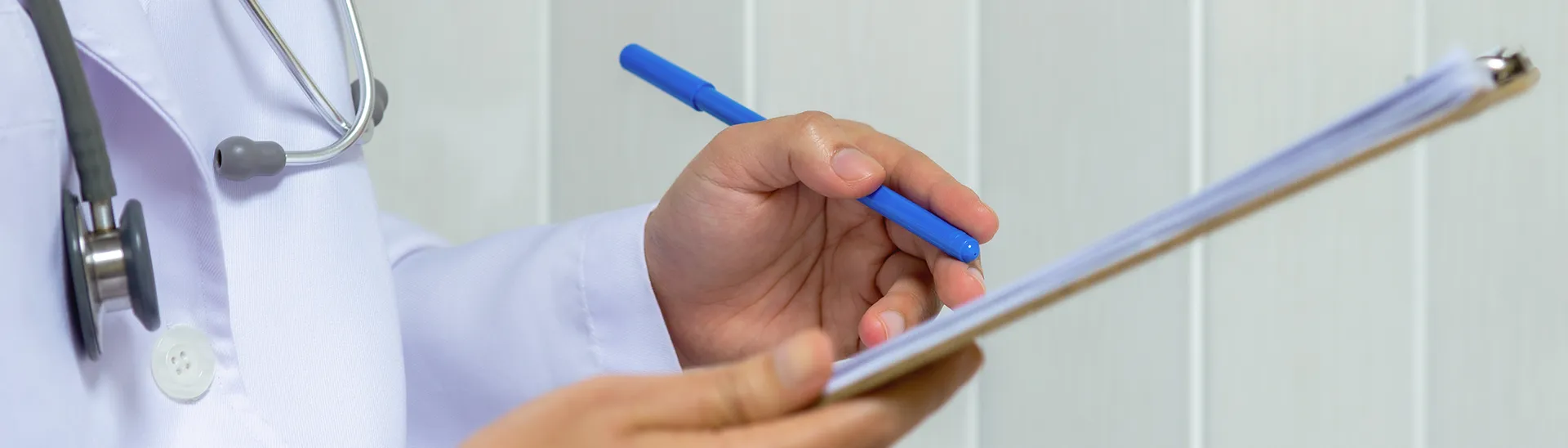 A doctor writing notes on a clipboard with a blue pen.